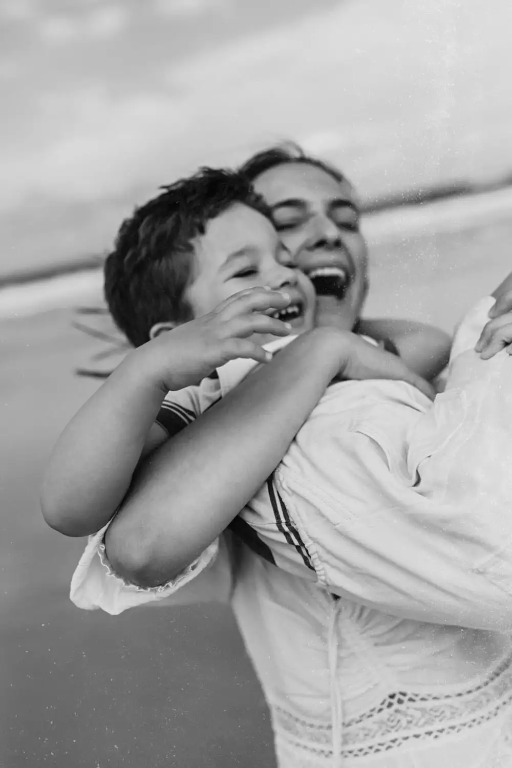 black and white image of mother and son laughing and playing on the beach